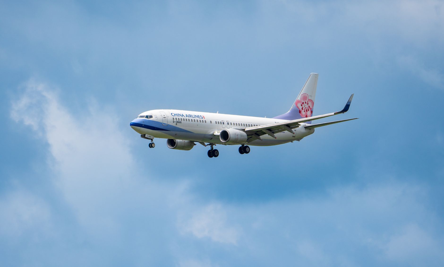 A China Airlines aircraft captured mid-flight against a bright blue sky with clouds.