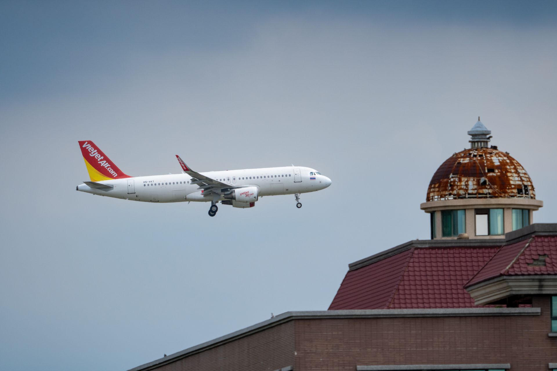 A VietJet Air airplane approaching landing over a building with a domed roof.