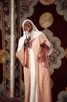 A Muslim woman in a pink robe speaking with a microphone.
