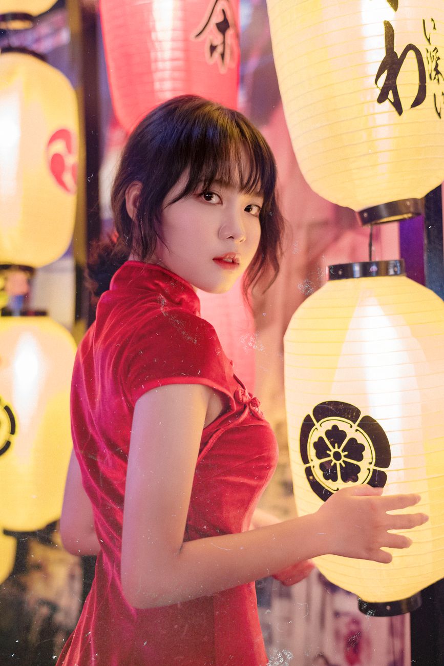 A woman stands by brightly lit Japanese lanterns wearing a red dress, creating a vibrant and cultural ambiance.