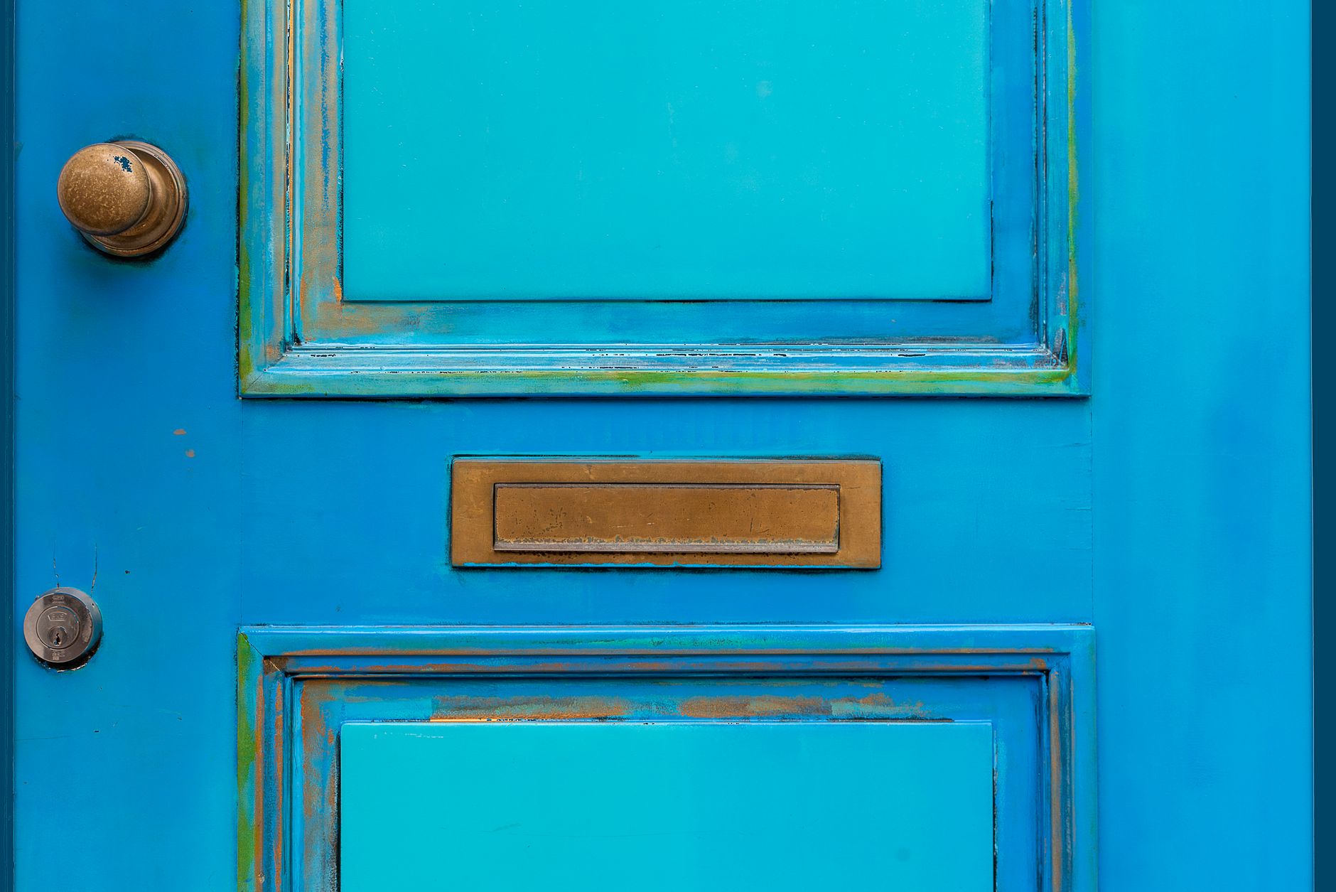 Close-up of a vintage blue wooden door featuring a brass mail slot and door knob.