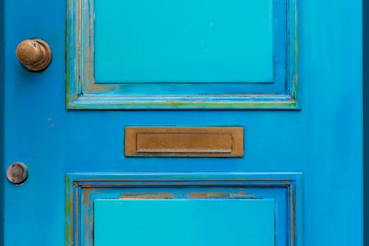 Close-up of a vintage blue wooden door featuring a brass mail slot and door knob.