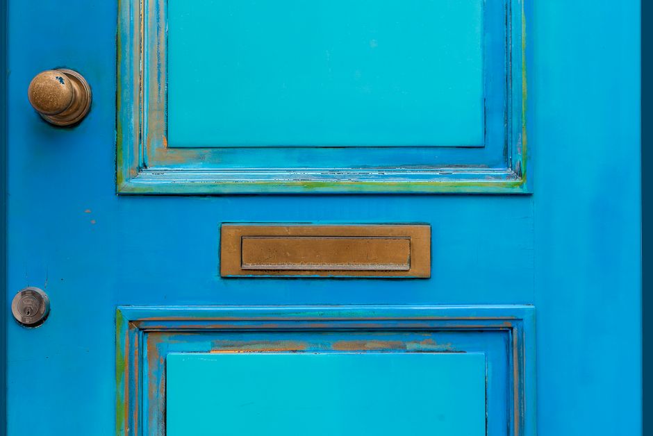 Close-up of a vintage blue wooden door featuring a brass mail slot and door knob.