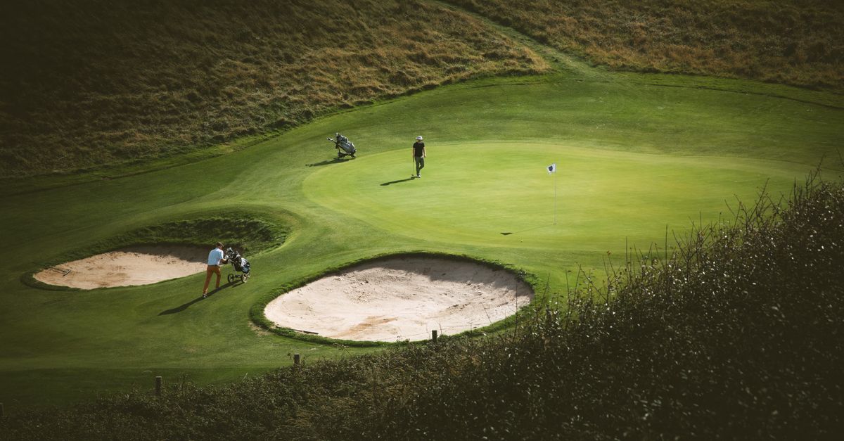 Golfers on a sunny day at Étretat Golf Course, France, surrounded by lush greens and sand traps.