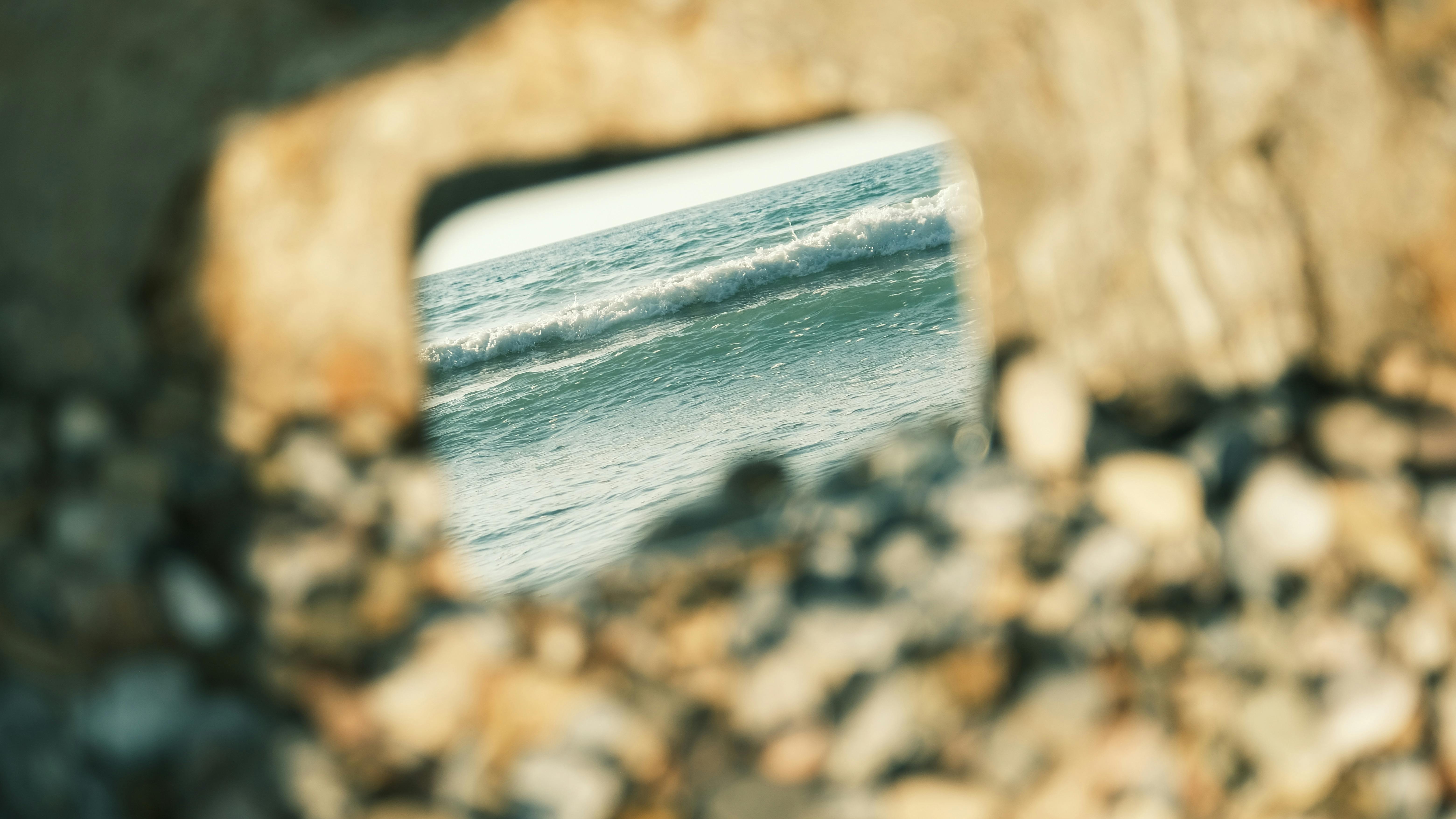 gratis Uitzicht op de golven van de oceaan, omlijst door een natuurlijke stenen opening in een kiezelstrand. Stockfoto