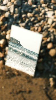 A mirror reflects ocean waves amidst pebbled beach, creating a unique visual contrast.