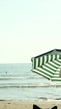 Green striped umbrella on a sunny beach day by the ocean's edge.