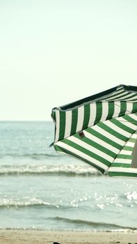 Green and white striped beach umbrella with ocean and blue sky in background.