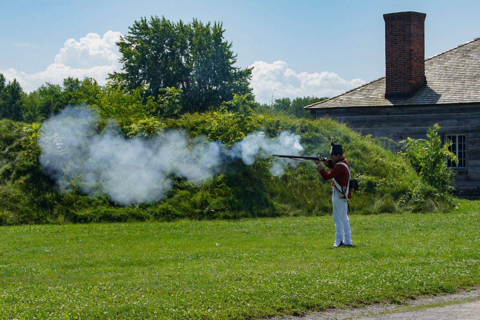 A historical reenactor in period uniform fires a musket, representing the soldiers who fought at Trenton