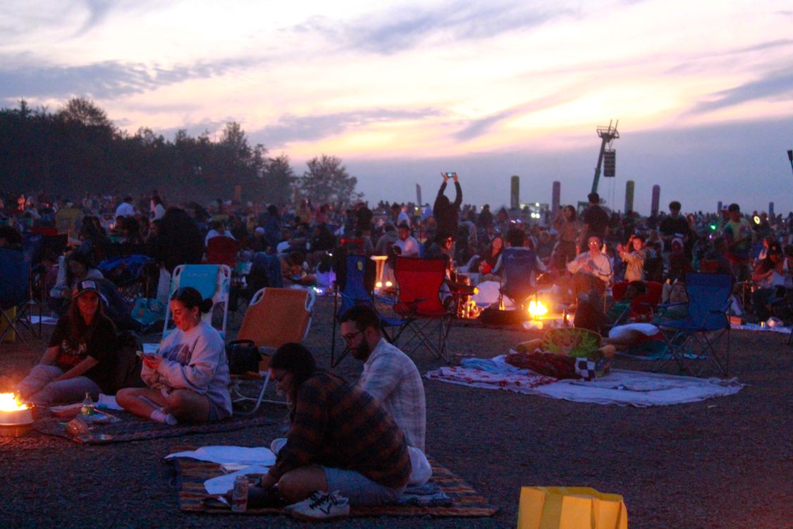 Free A vibrant scene of people enjoying an outdoor music festival at sunset, with camping chairs and fire pits. Stock Photo