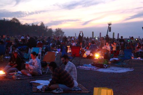 Free A vibrant scene of people enjoying an outdoor music festival at sunset, with camping chairs and fire pits. Stock Photo