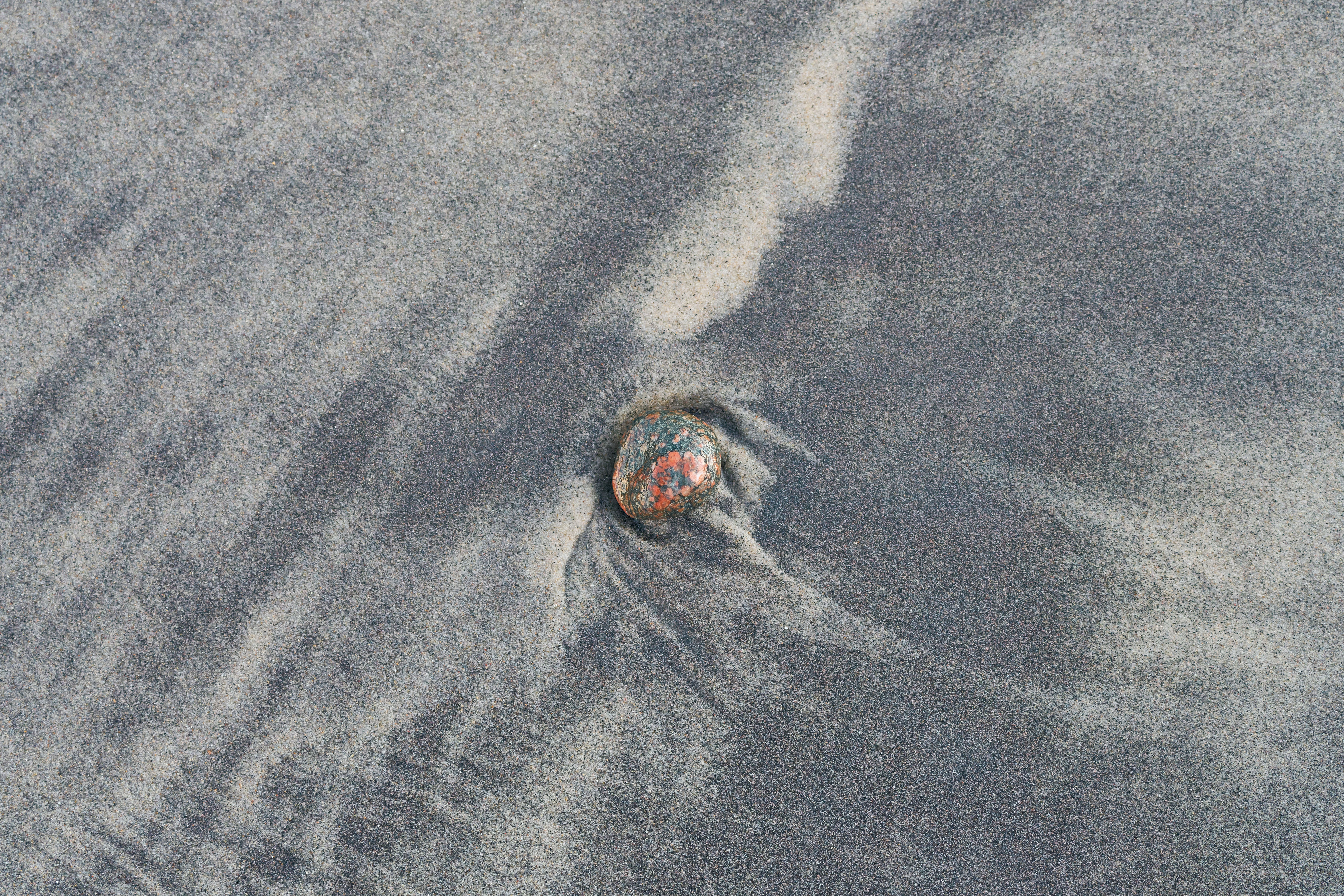 A smooth pebble set amidst unique sand patterns on a beach.