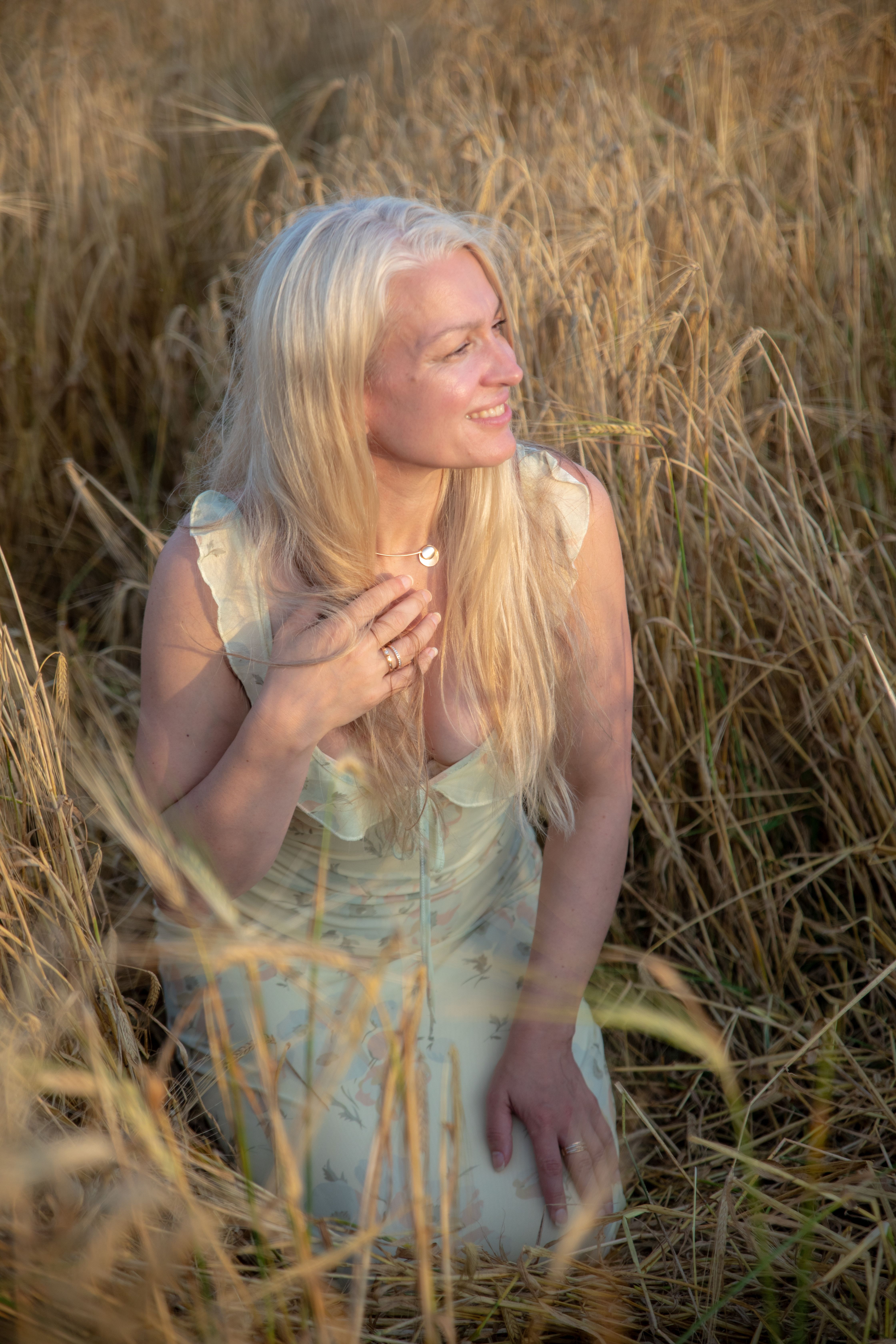 Blonde woman in a wheat field enjoying the sunset. Captures nature's warmth and serenity.