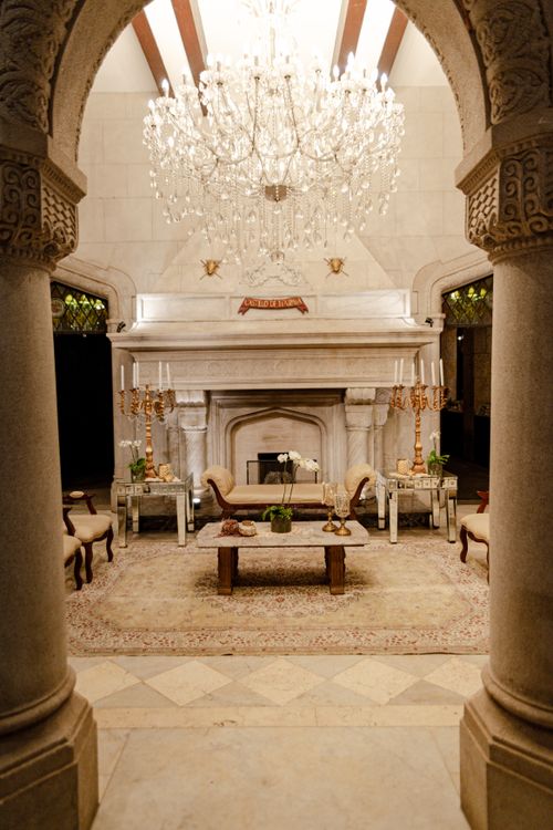 Free Luxurious and elegant medieval castle interior featuring a grand chandelier over an intricate fireplace setup. Stock Photo