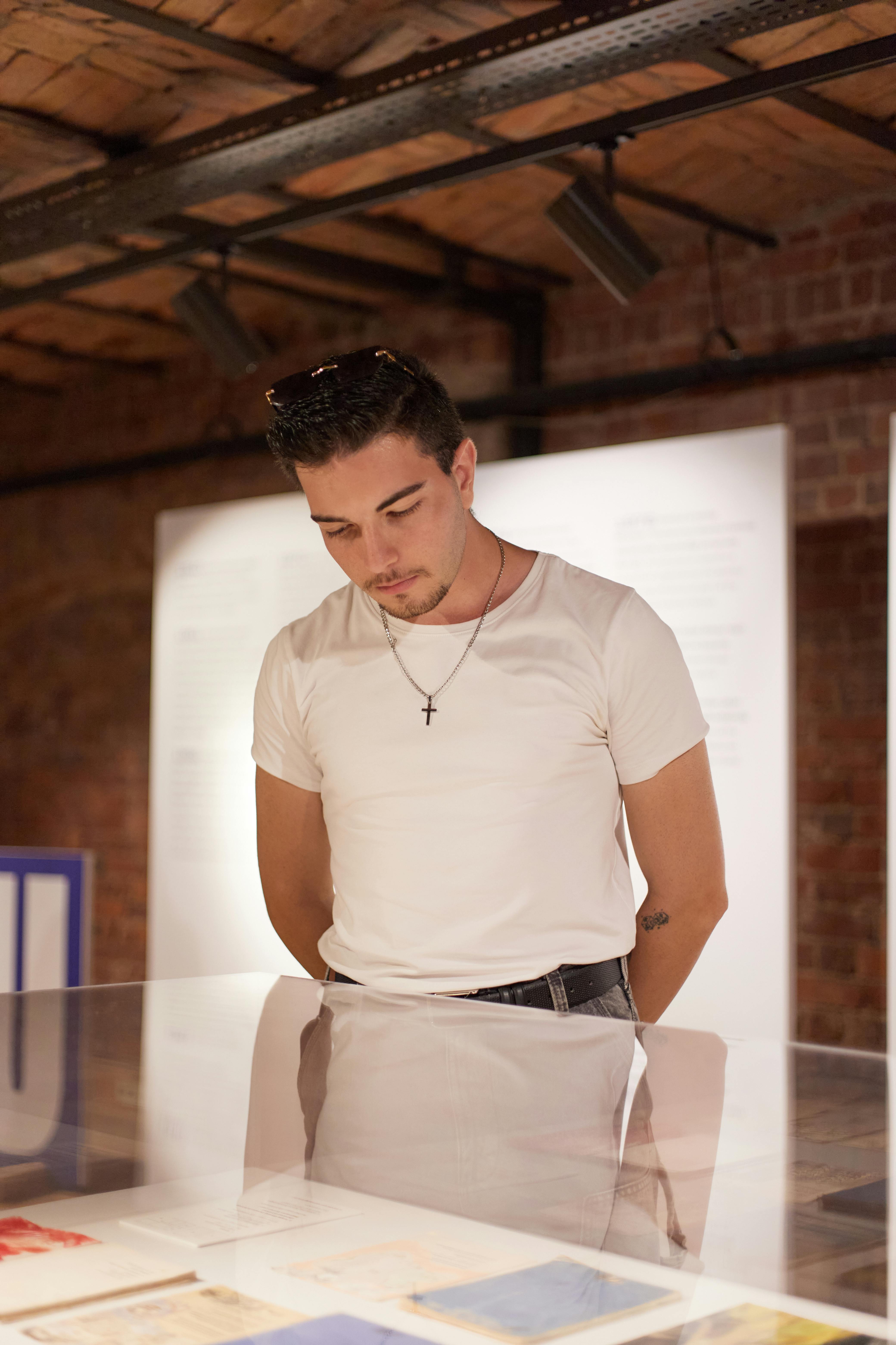 A young man wearing a white shirt and necklace, attentively examining a museum display case in Istanbul.
