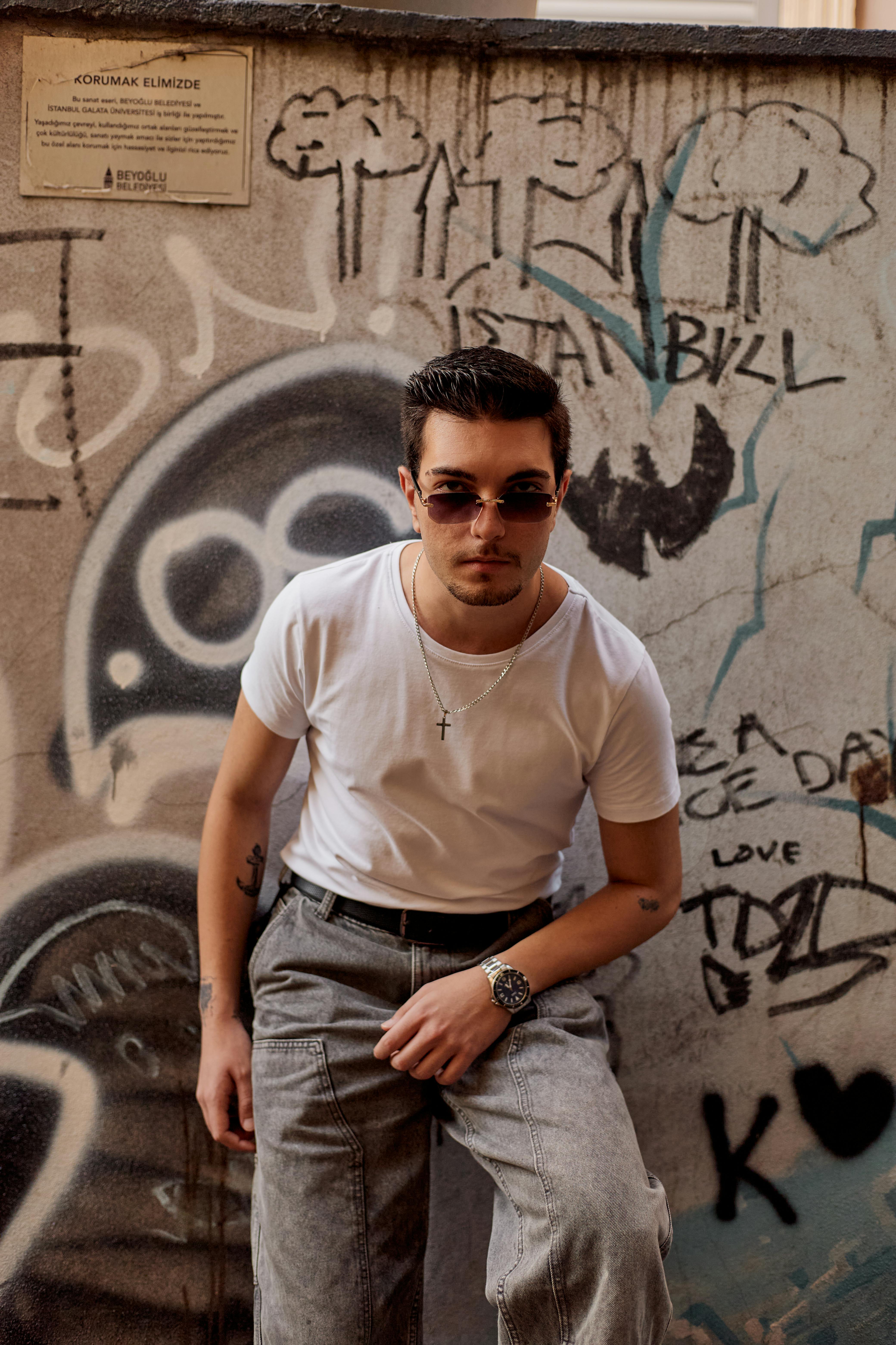 Stylish young man in sunglasses poses confidently against a graffiti-covered wall in İstanbul.