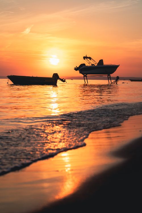 Free Peaceful sunset scene with boats on still water reflecting vivid orange sky tones. Stock Photo