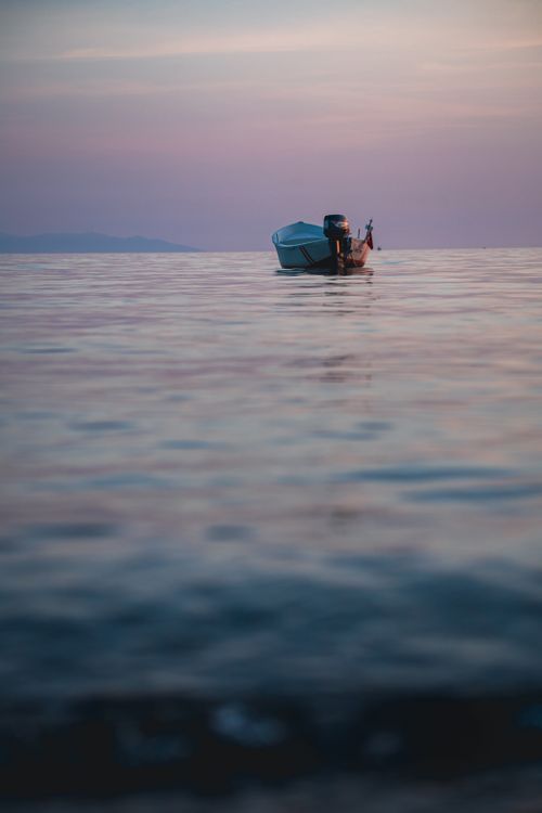 Free Lone boat on a calm sea during a tranquil sunset with pastel skies reflecting on the water. Stock Photo