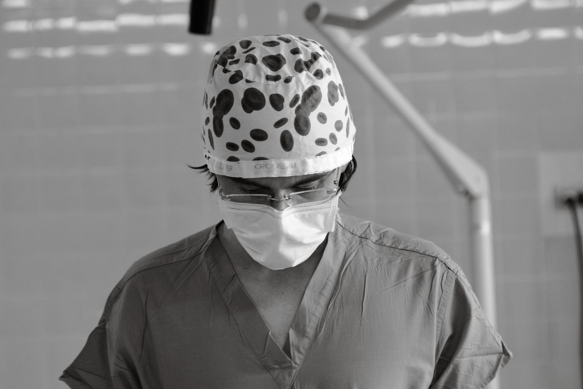 Black and white photo of a focused surgeon wearing scrubs and mask in the operating room.