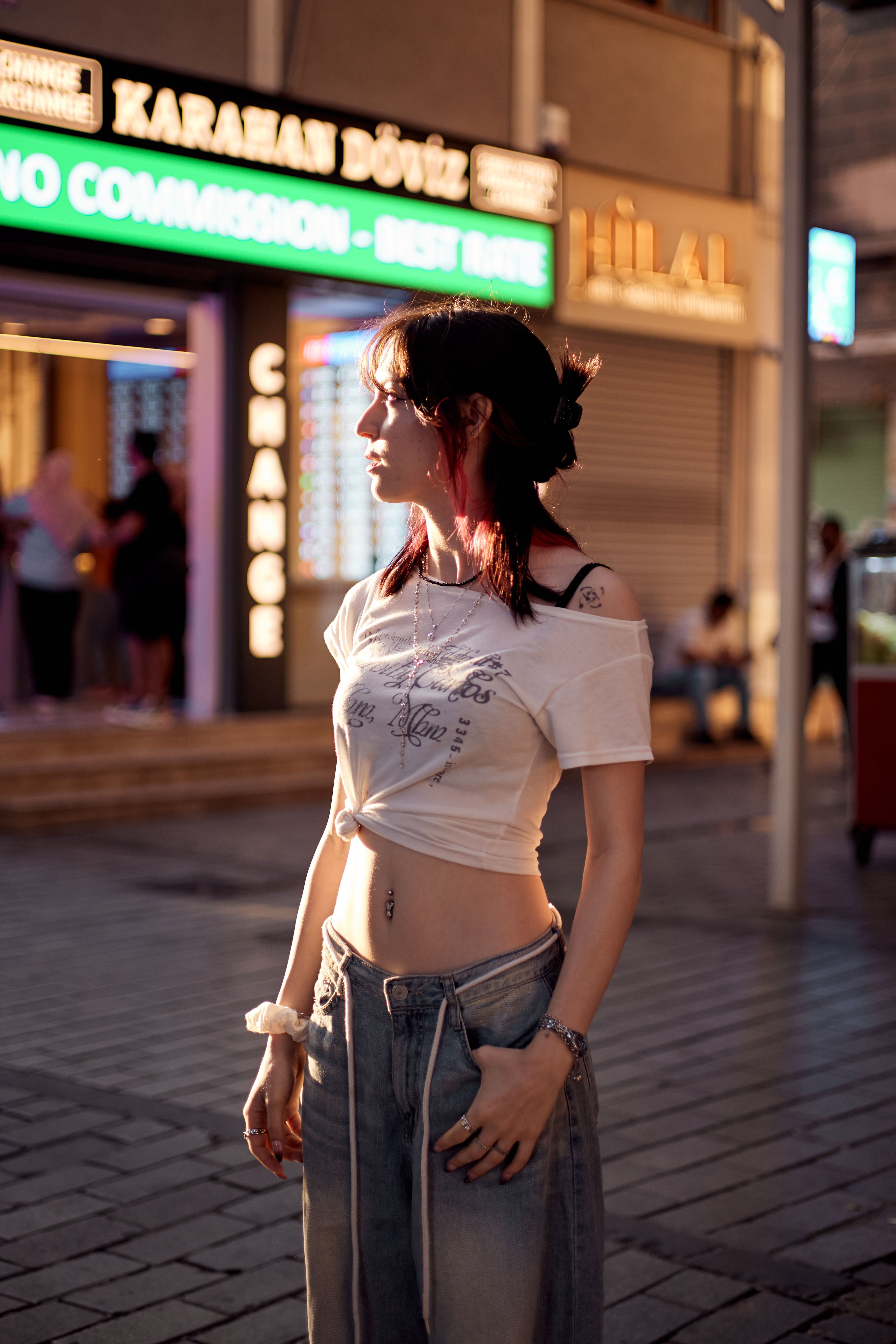 A young woman with a trendy style strolls through an illuminated street in İstanbul, Türkiye at twilight.