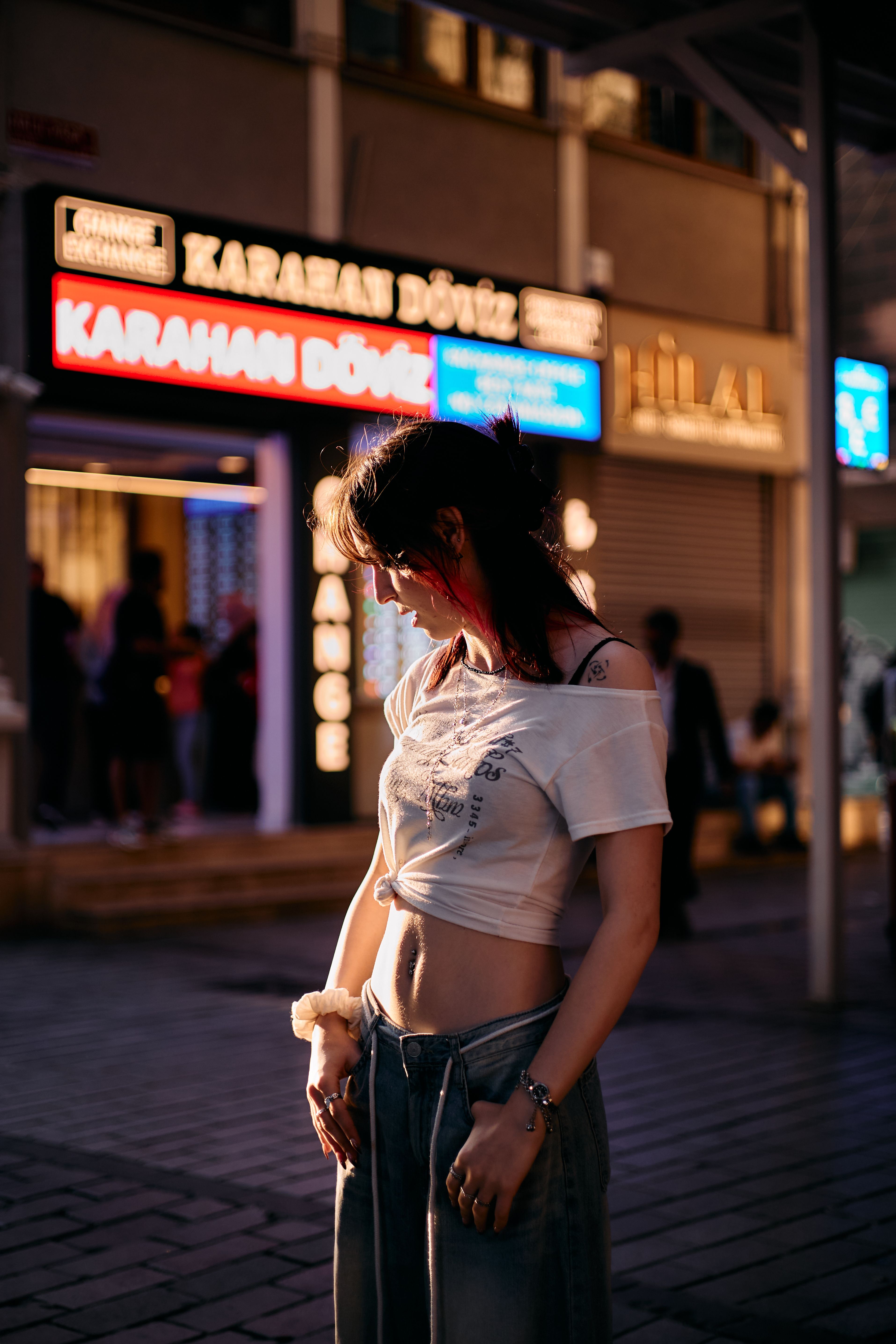 A young woman in casual attire stands in an evening street scene in Istanbul, illuminated by vibrant neon lights.