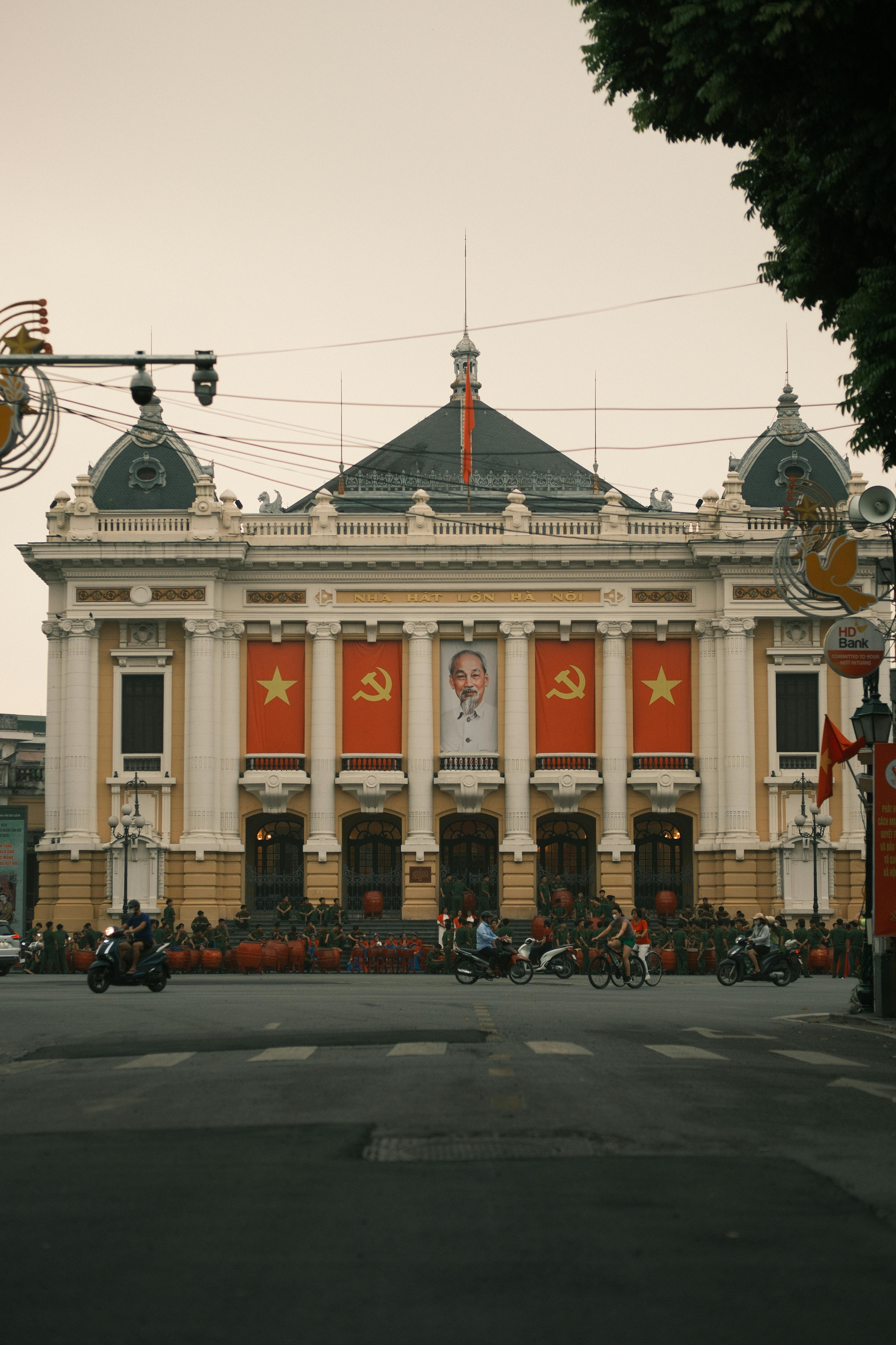 Gratis Edificio in stile coloniale ad Hanoi decorato con bandiere e ritratti, vivace scena di strada con motociclette. Foto a disposizione