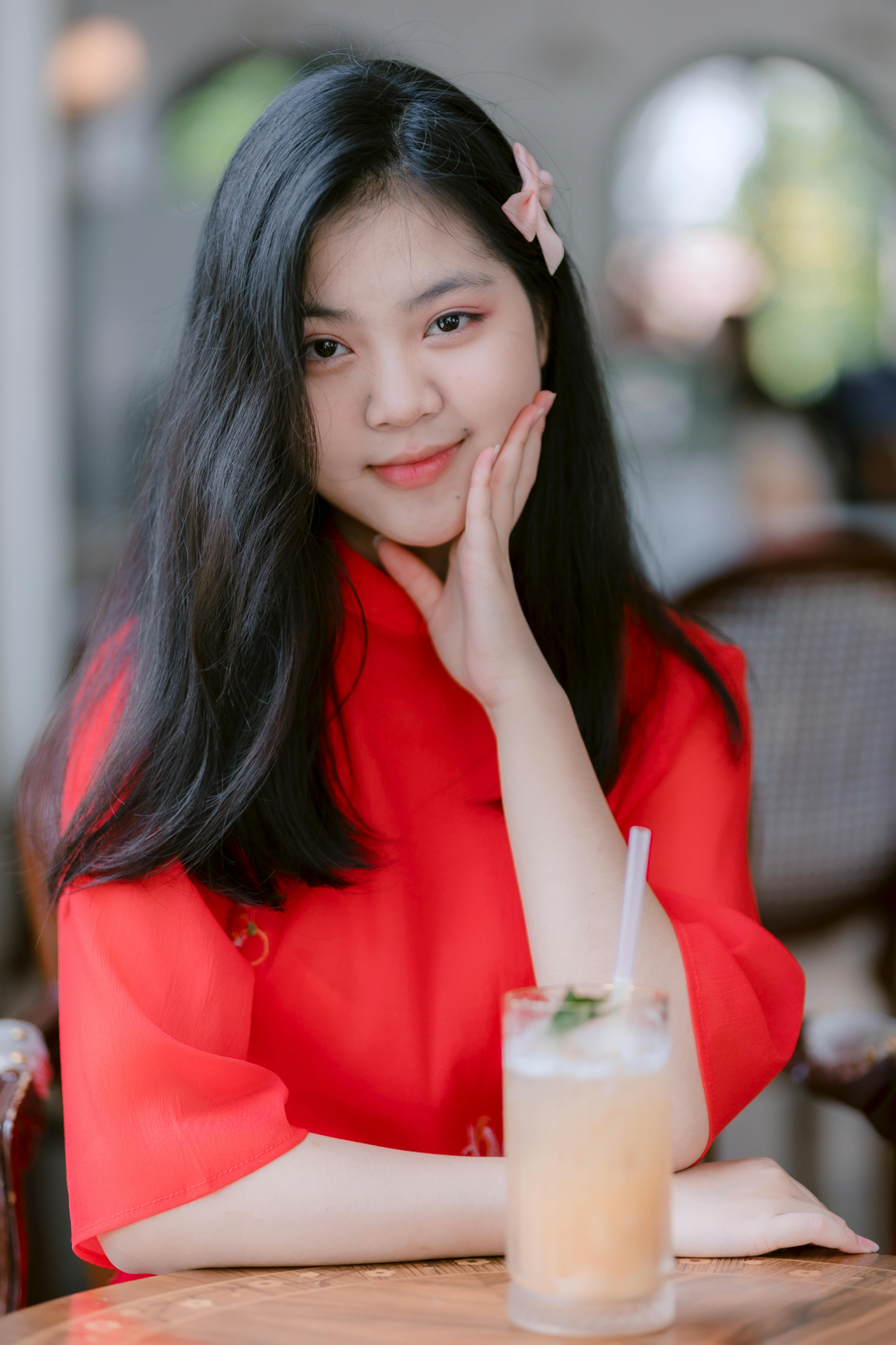 Elegant young woman in red enjoying a drink at a cafe. Serene and joyful atmosphere.