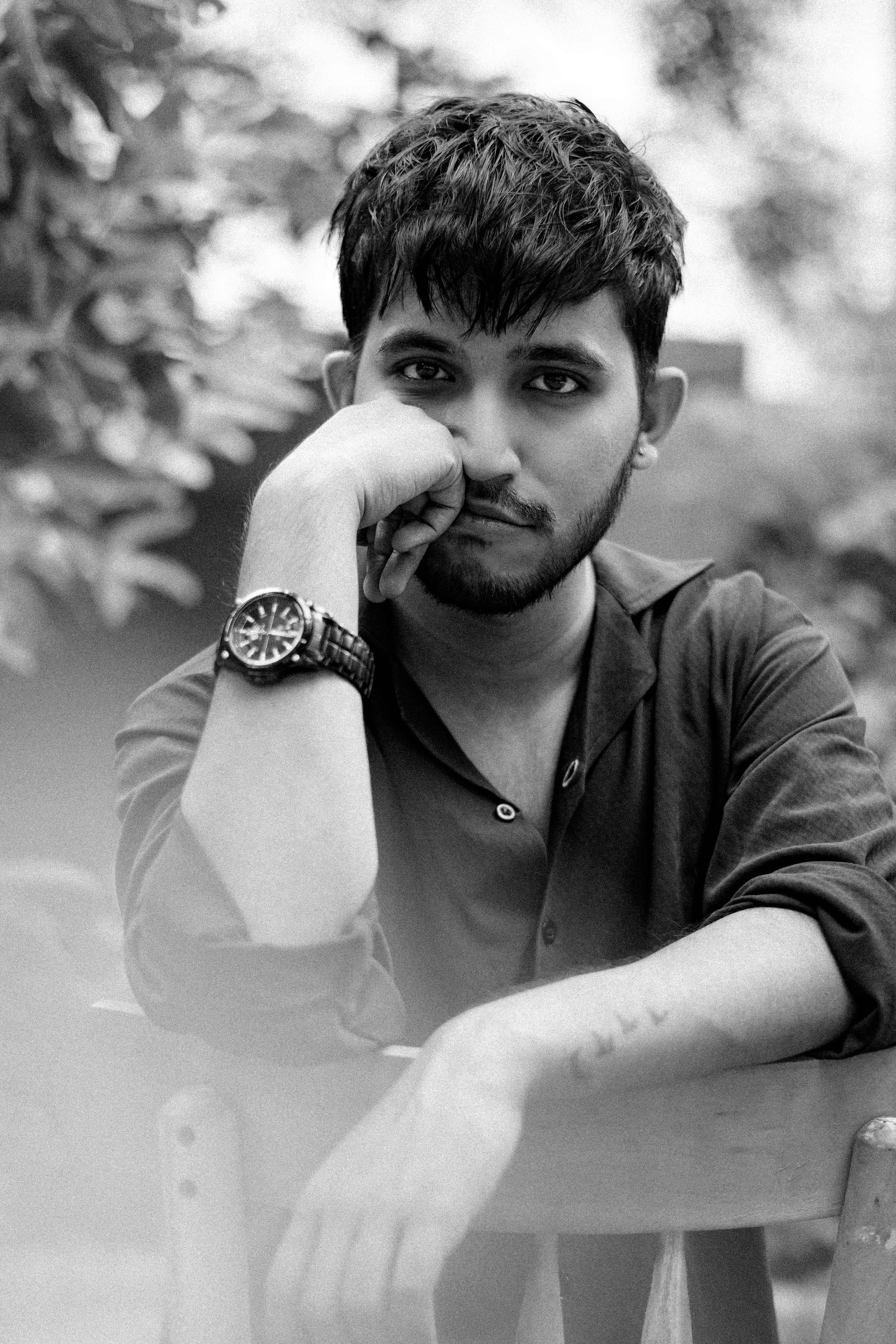 Black and white portrait of a young man in a thoughtful pose, sitting outdoors.