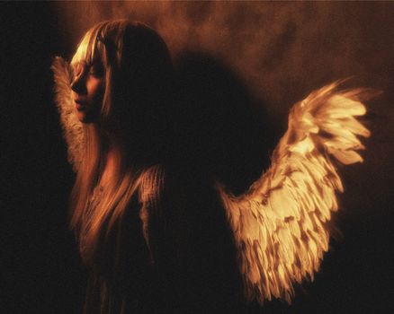 Moody portrait of an angelic figure with glowing wings, evoking mystery and serenity.