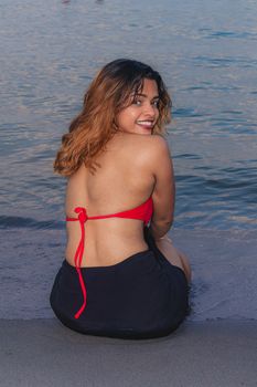 Smiling woman in a red bikini sitting by the water on a calm Toronto evening.