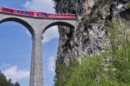 Stunning view of a red train crossing the Landwasser Viaduct in the Swiss Alps, framed by rocky cliffs.