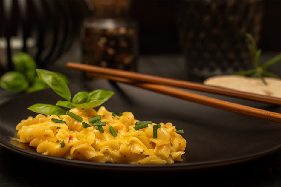 Delicious creamy pasta garnished with basil and chives, served on a black plate with chopsticks.