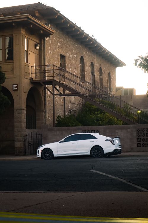 Free A sleek white car parked next to a vintage stone building during daylight. Stock Photo