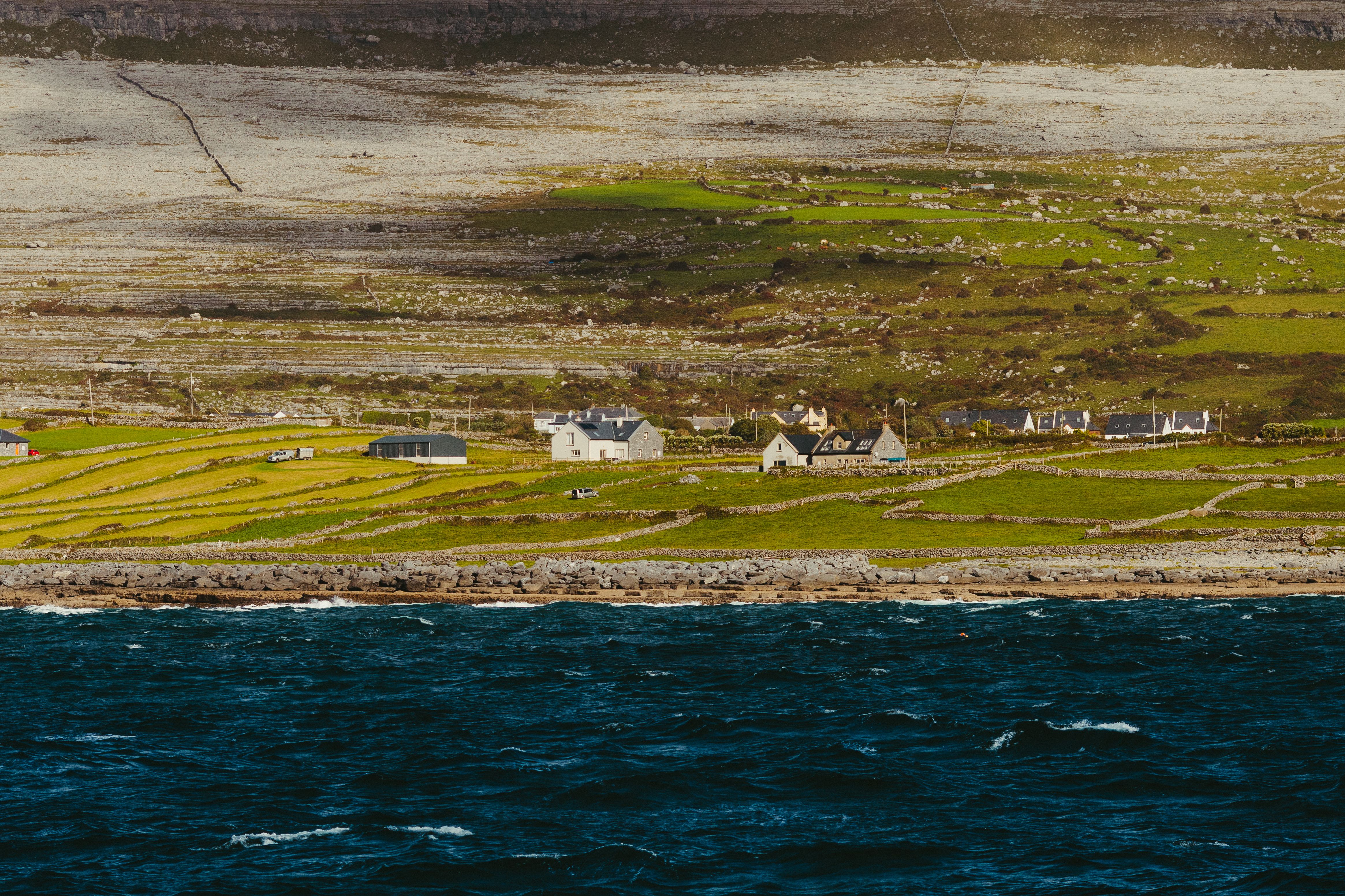 Picturesque coastal view of Inishmore, County Galway, showcasing lush fields and traditional stone cottages under a clear sky.