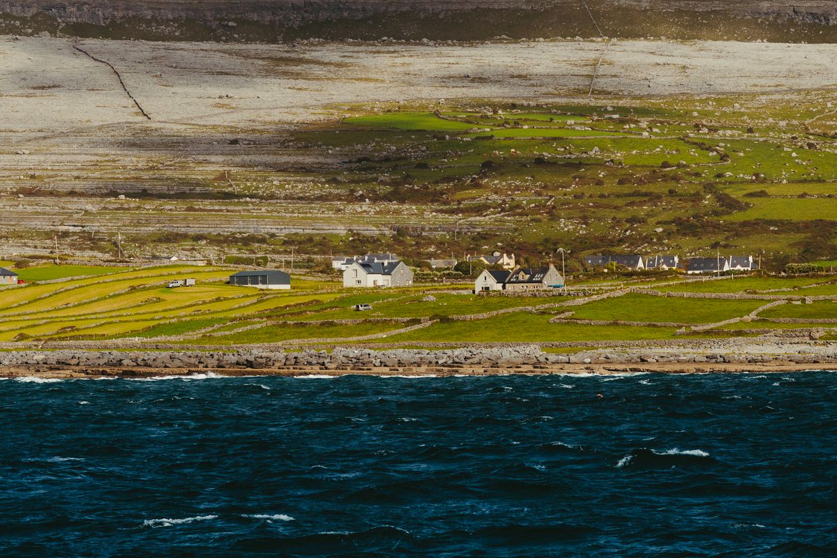 Picturesque coastal view of Inishmore, County Galway, showcasing lush fields and traditional stone cottages under a clear sky.