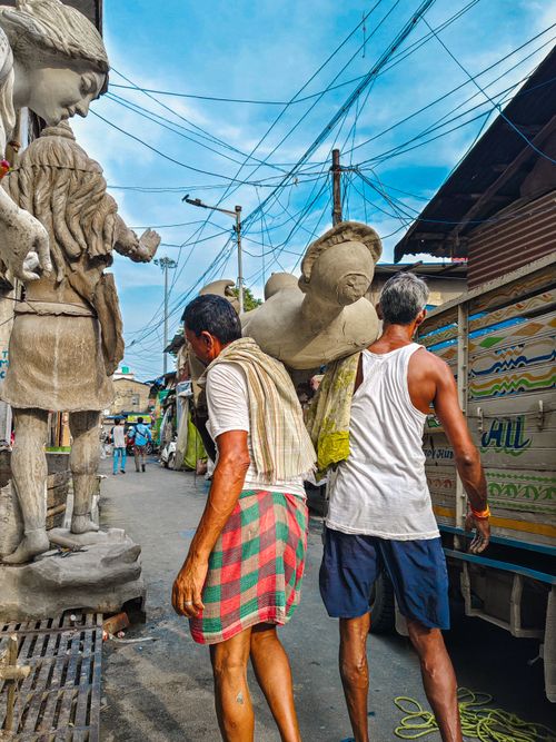 Free Artisans carry large sculptures through a vibrant outdoor market. A dynamic mix of tradition and culture. Stock Photo