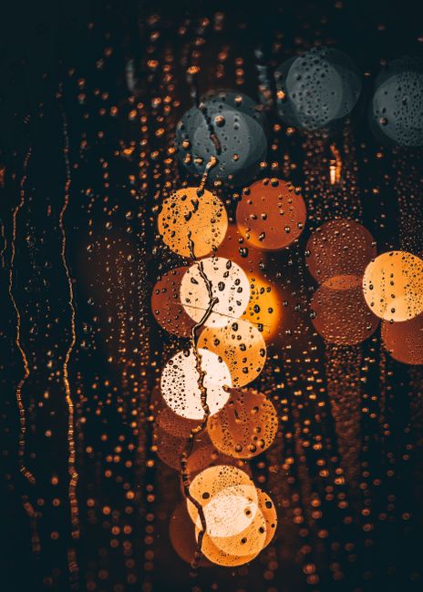 Abstract view of colorful bokeh lights through a rainy window, creating a warm, moody atmosphere.