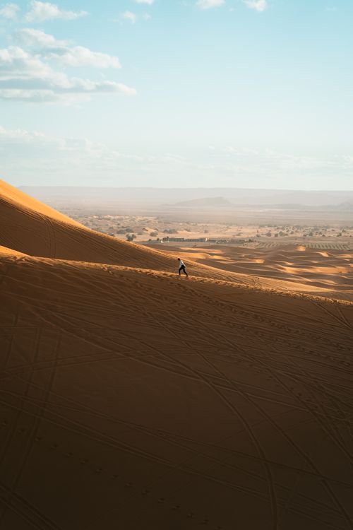 Free A lone person walking on vast golden sand dunes under a clear sky. Stock Photo