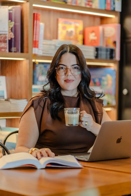 Free Woman in bookstore enjoying coffee while working on a laptop, conveying a cozy, modern lifestyle. Stock Photo