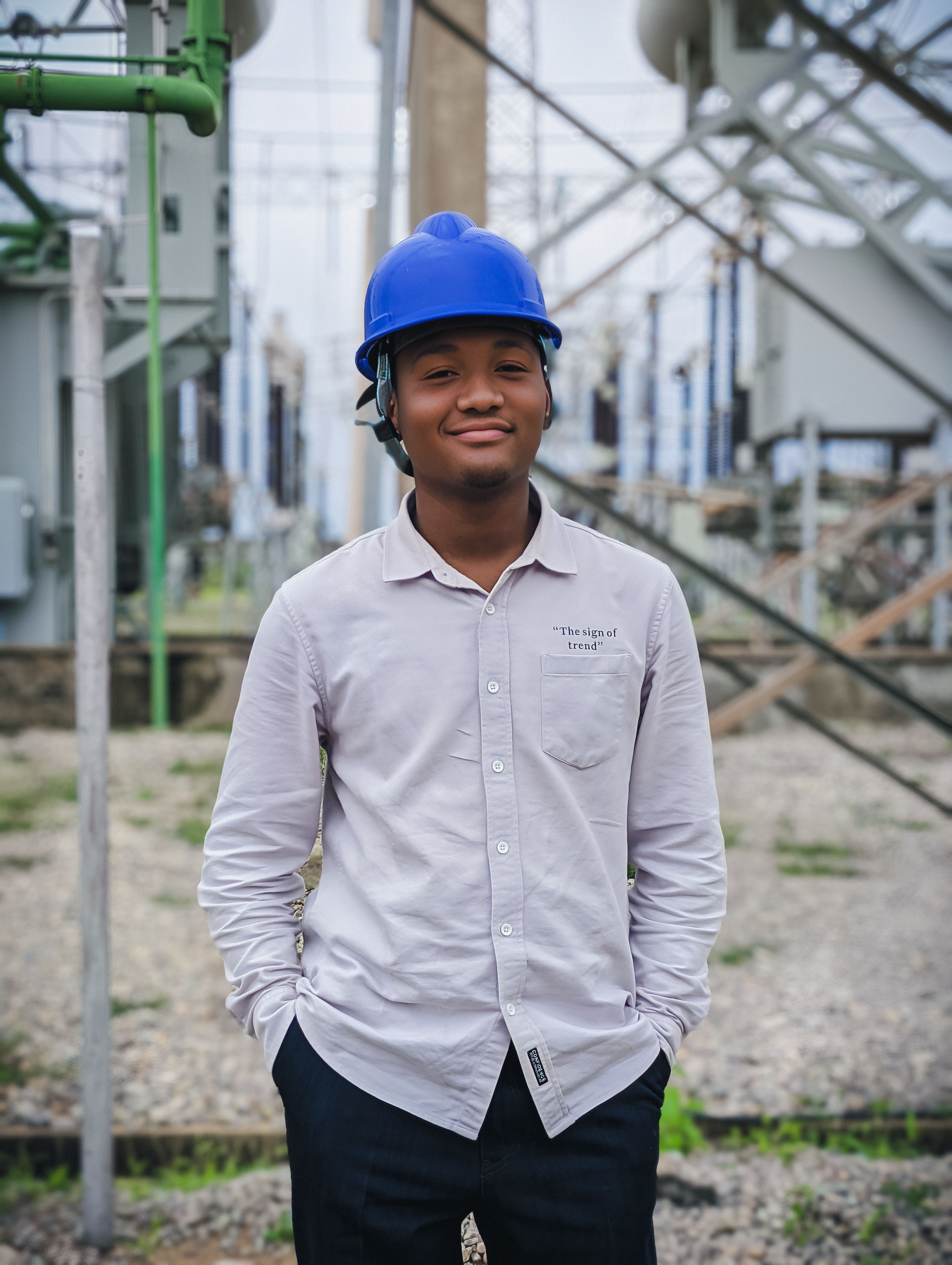 A young engineer wearing a hard hat stands at an electrical substation in Kaduna, Nigeria.