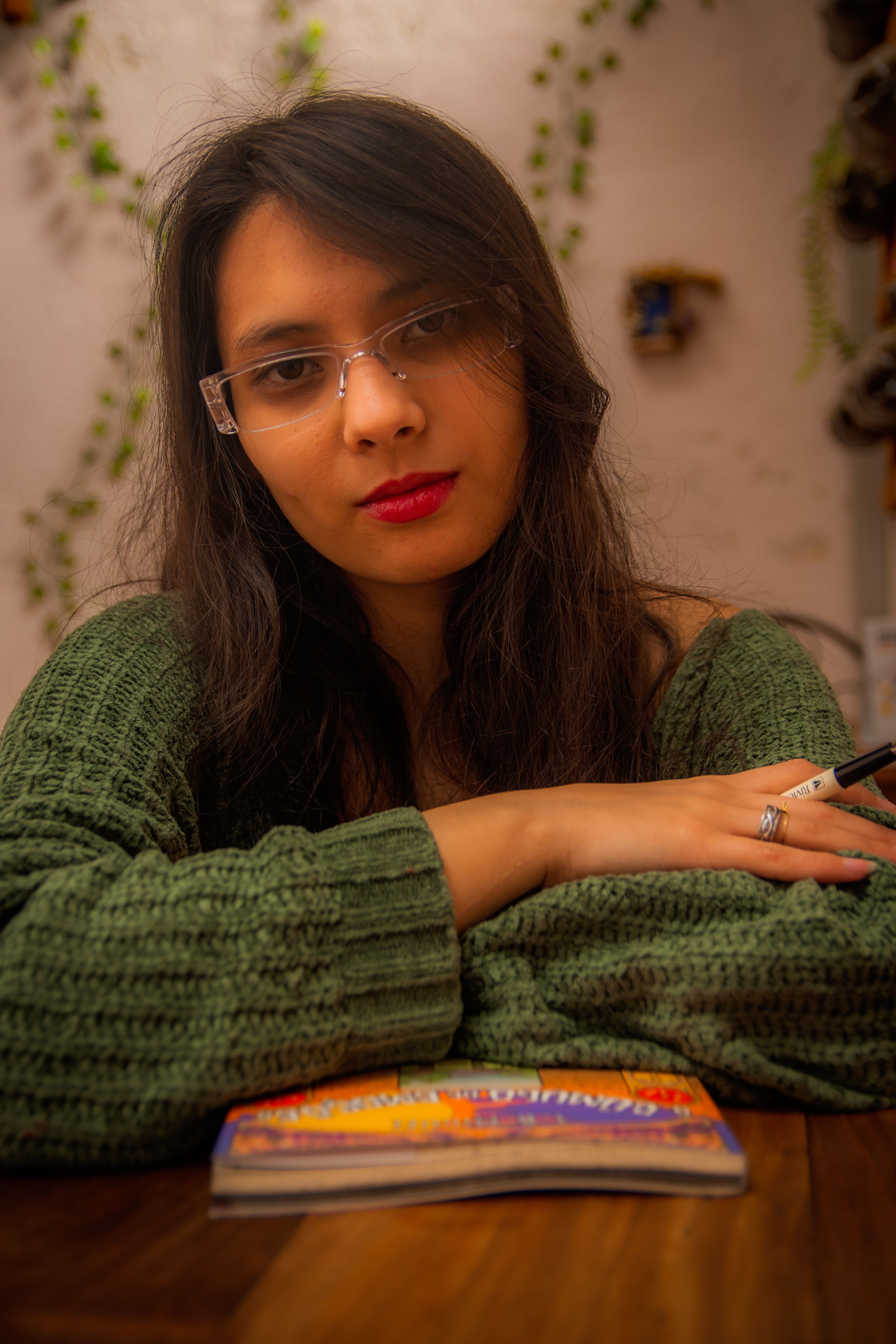 Portrait of a woman with glasses reading a book at a wooden table in a cozy indoor setting with warm lighting.