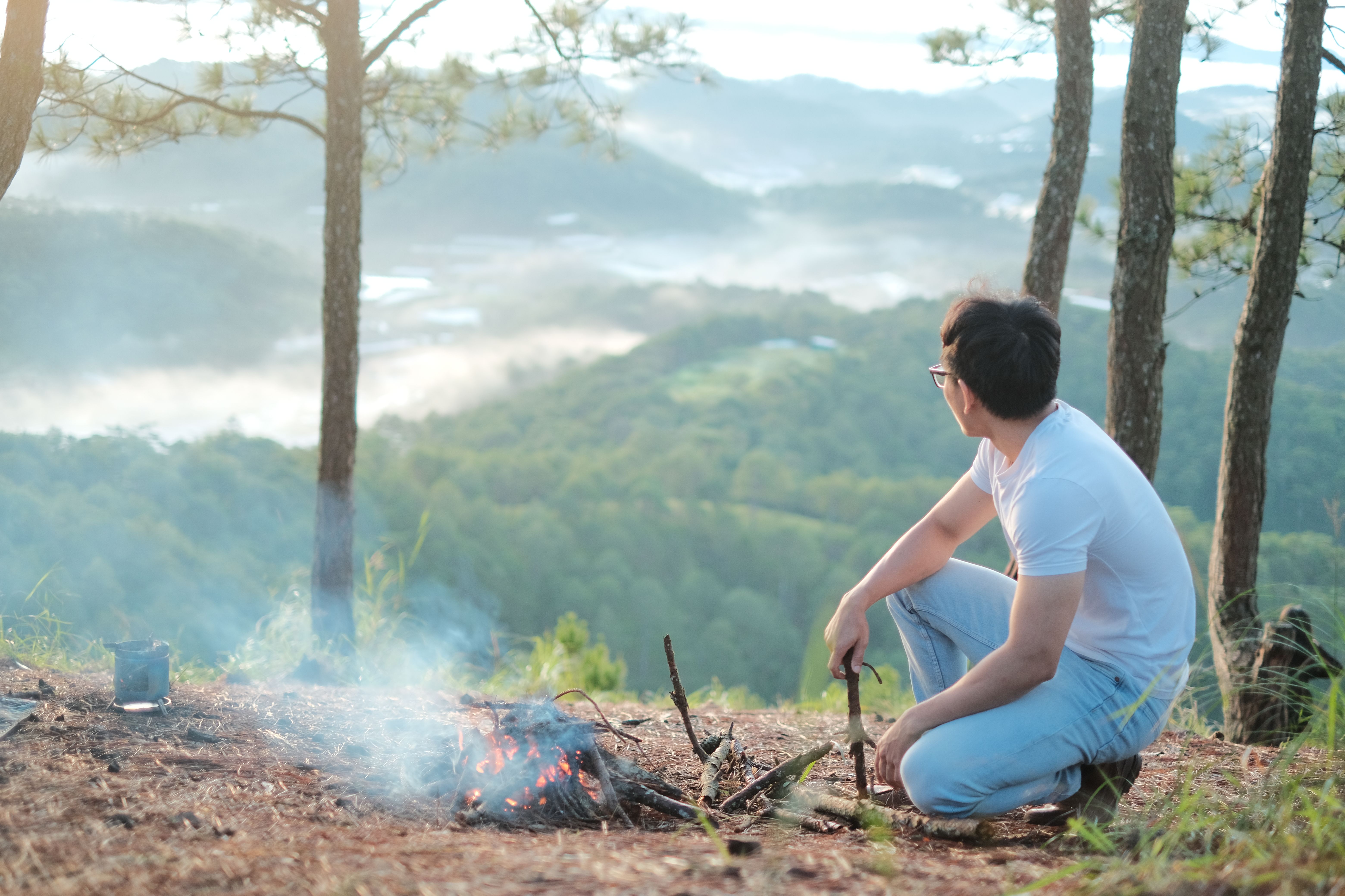 Man sitting by a campfire on a mountain, enjoying a scenic view.