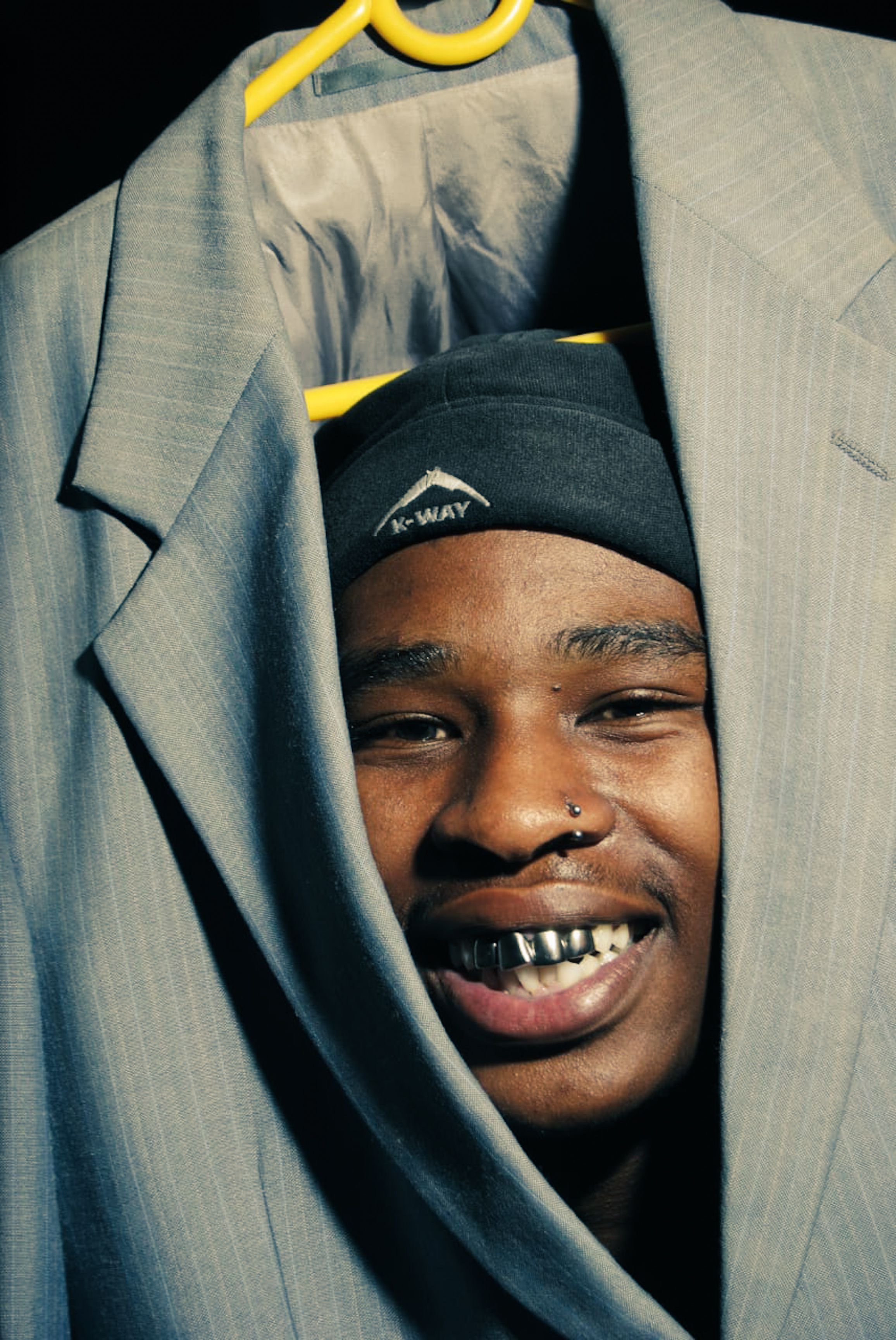 A cheerful man with a nose ring smiles while posing with a suit jacket.