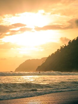Beautiful sunset over a tropical Costa Rica beach with waves crashing and scenic mountains.