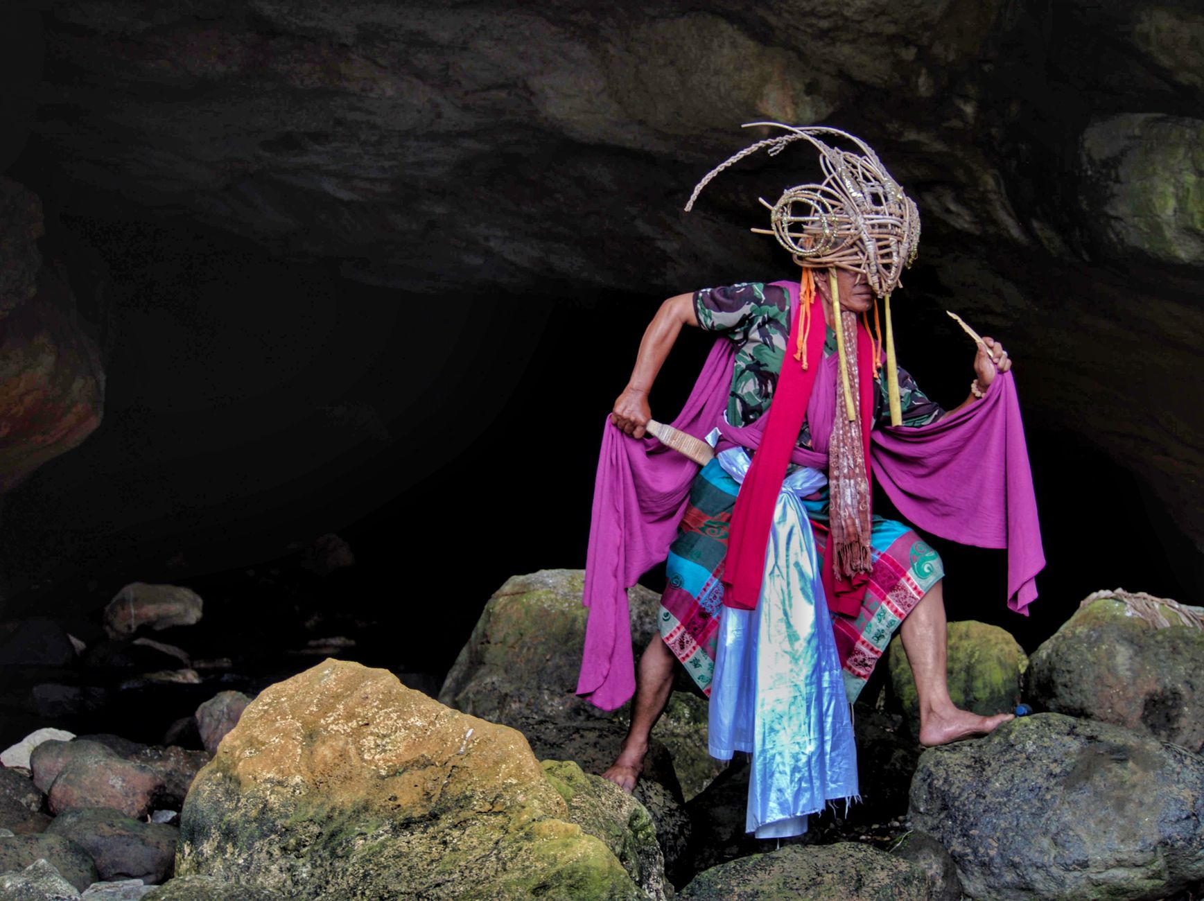 A traditional performer in vibrant attire poses dramatically inside a cave in West Java, Indonesia.