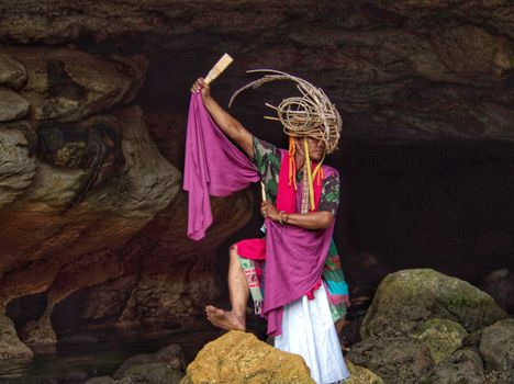 A person in vibrant traditional attire performing cultural gestures in a West Java cave.