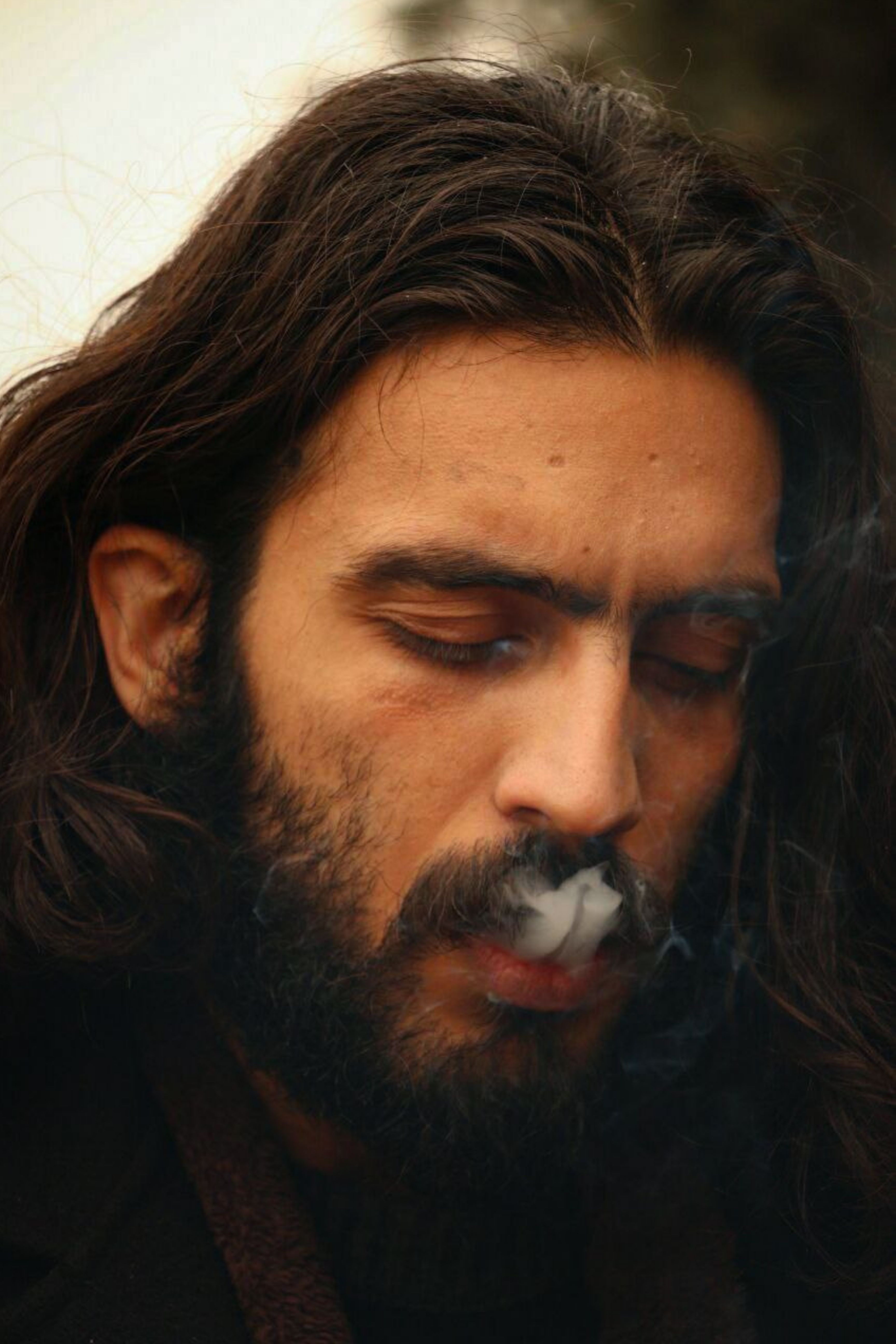 Close-up portrait of a Middle Eastern man smoking outdoors, capturing contemplative expression.