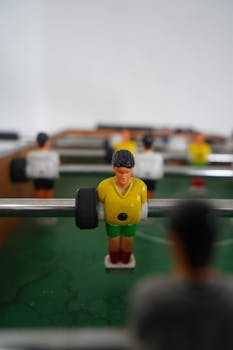 Detailed focus on a foosball player in a yellow jersey and green shorts on a green foosball table.