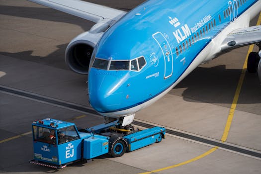 KLM airplane being towed with ground support vehicle on a sunny day at the airport.