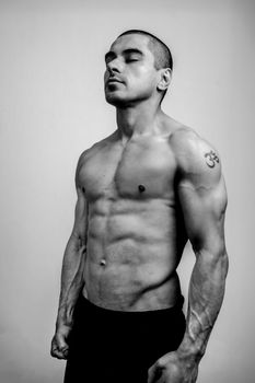 Powerful black and white portrait of a muscular man with a tattoo in a contemplative pose.